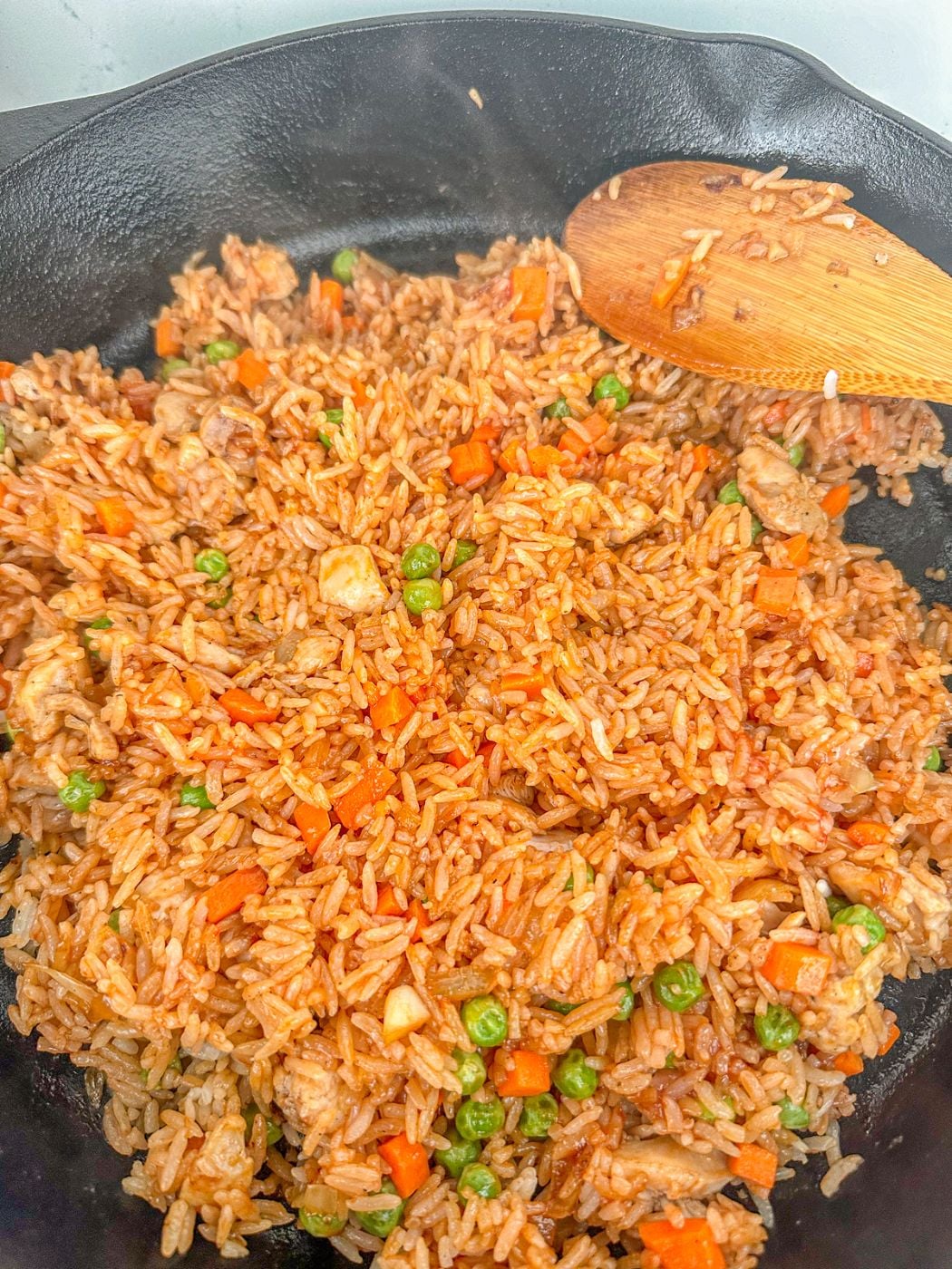 Mixing fried rice with ketchup, chicken, peas and carrots in a pan.