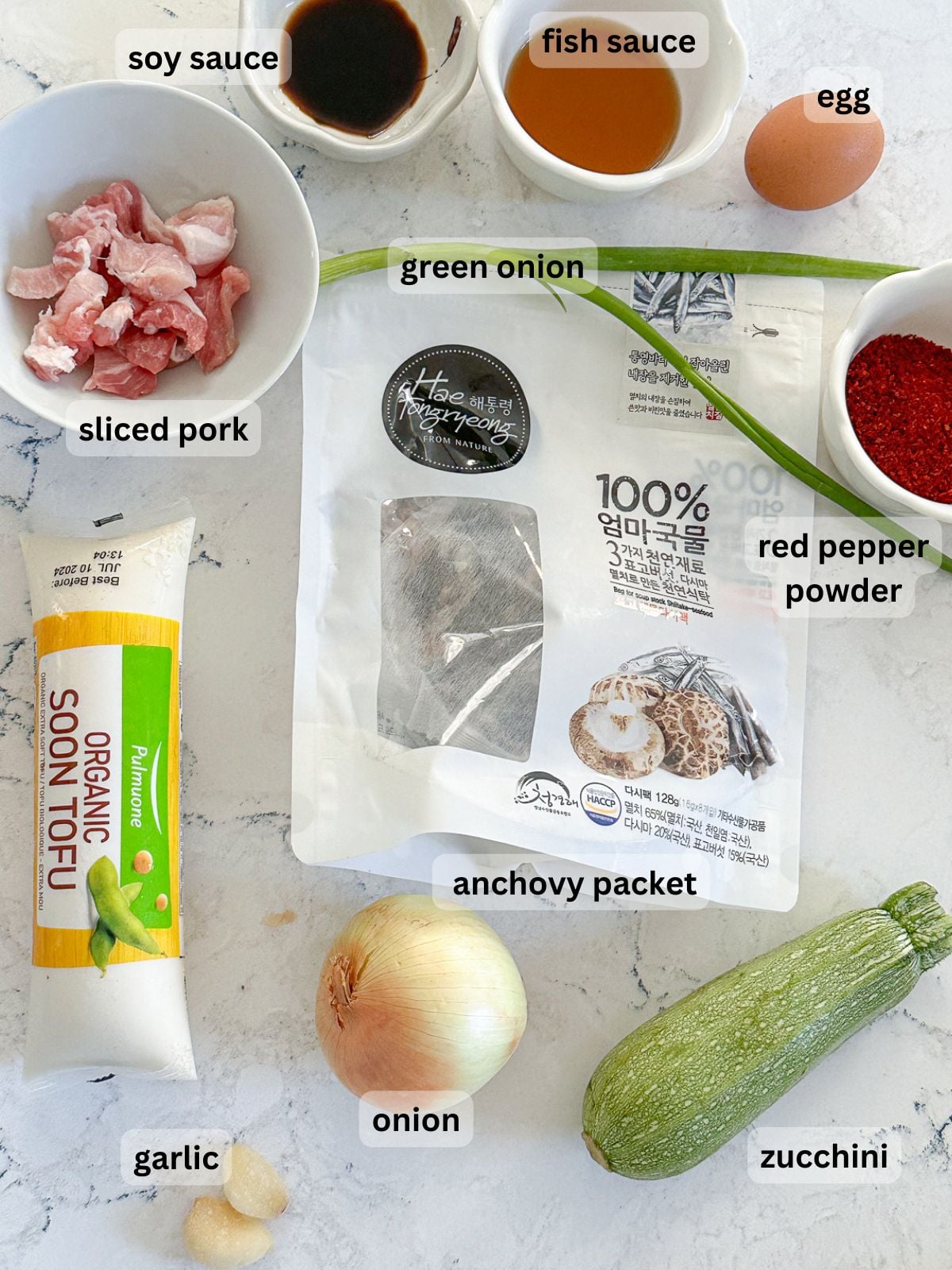 Ingredients include soy sauce, fish sauce, egg, green onion, red pepper powder, anchovy packet, onion, garlic, zucchini, soft tofu and sliced pork.