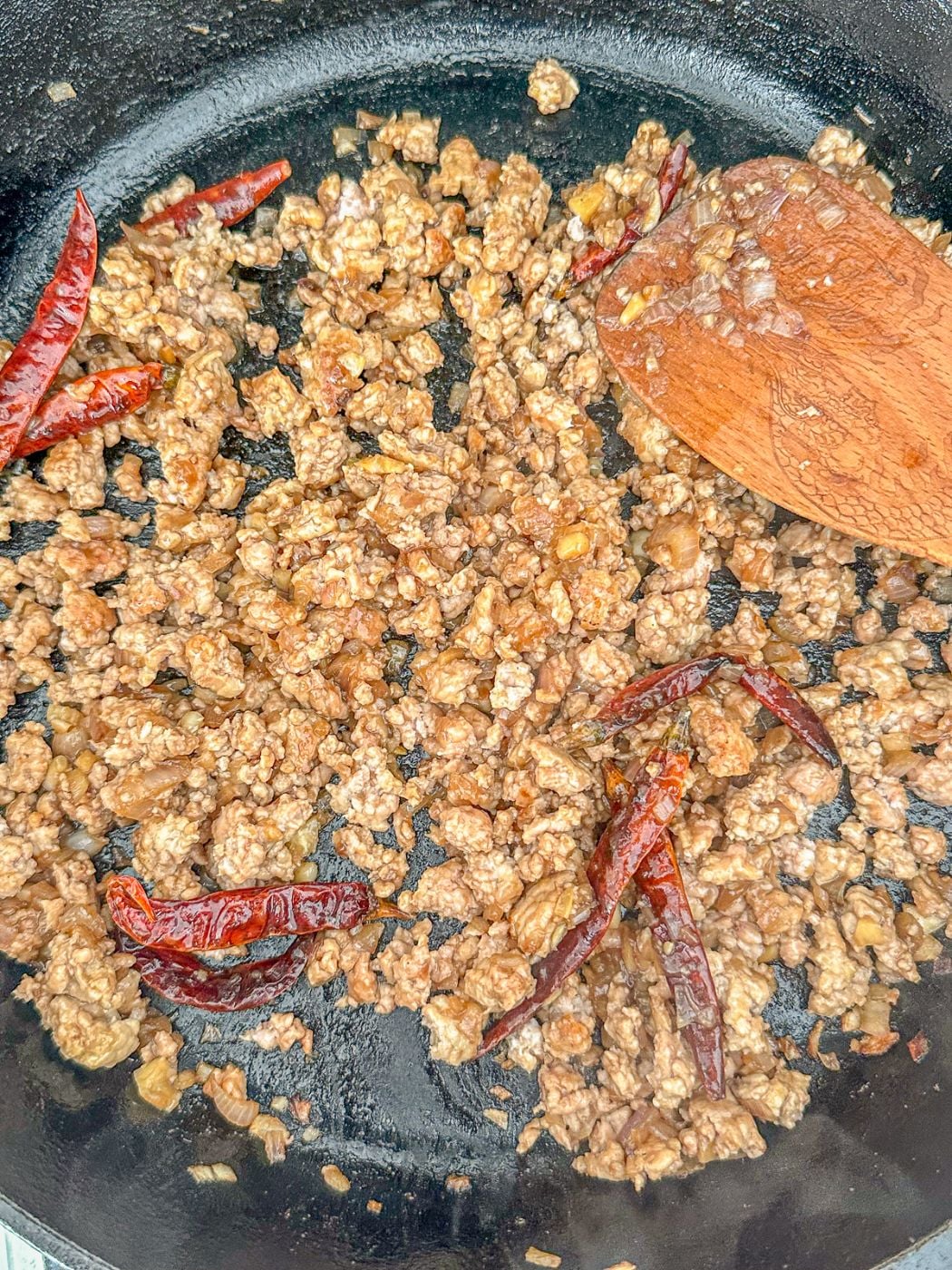 Minced pork in a skillet with with chili peppers.