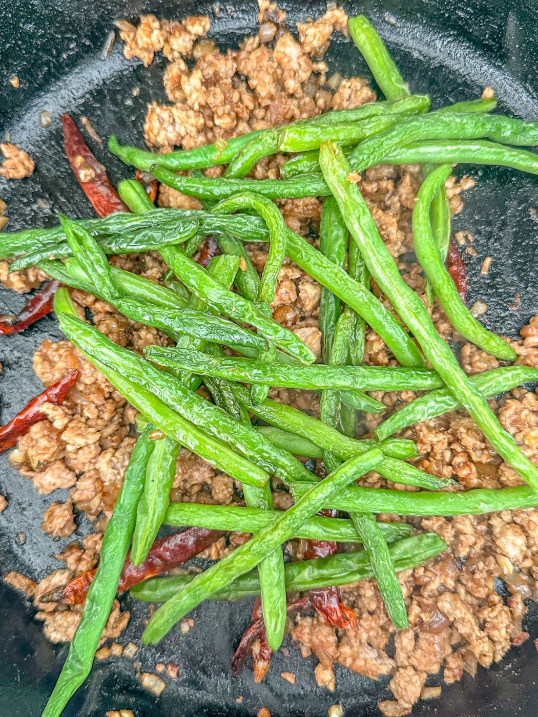 Green beans are added to the ground pork in the skillet.