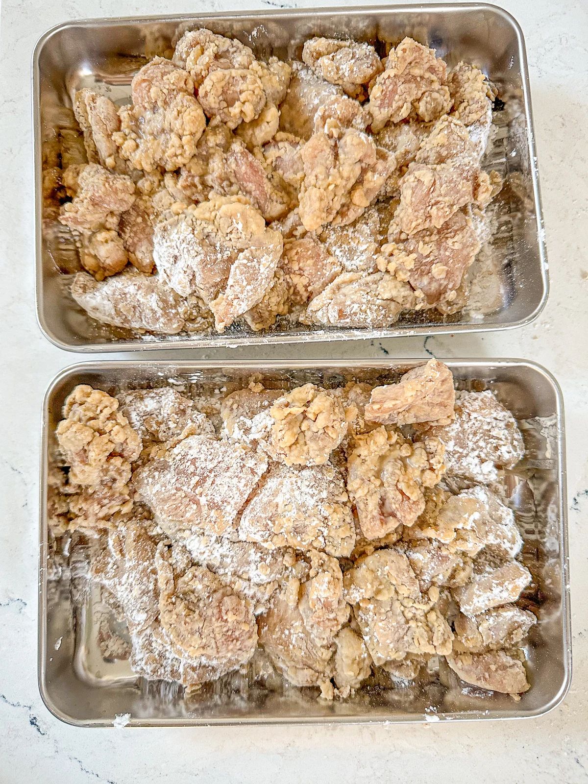 Two trays of chicken pieces coated in tapioca flour, ready for air frying.