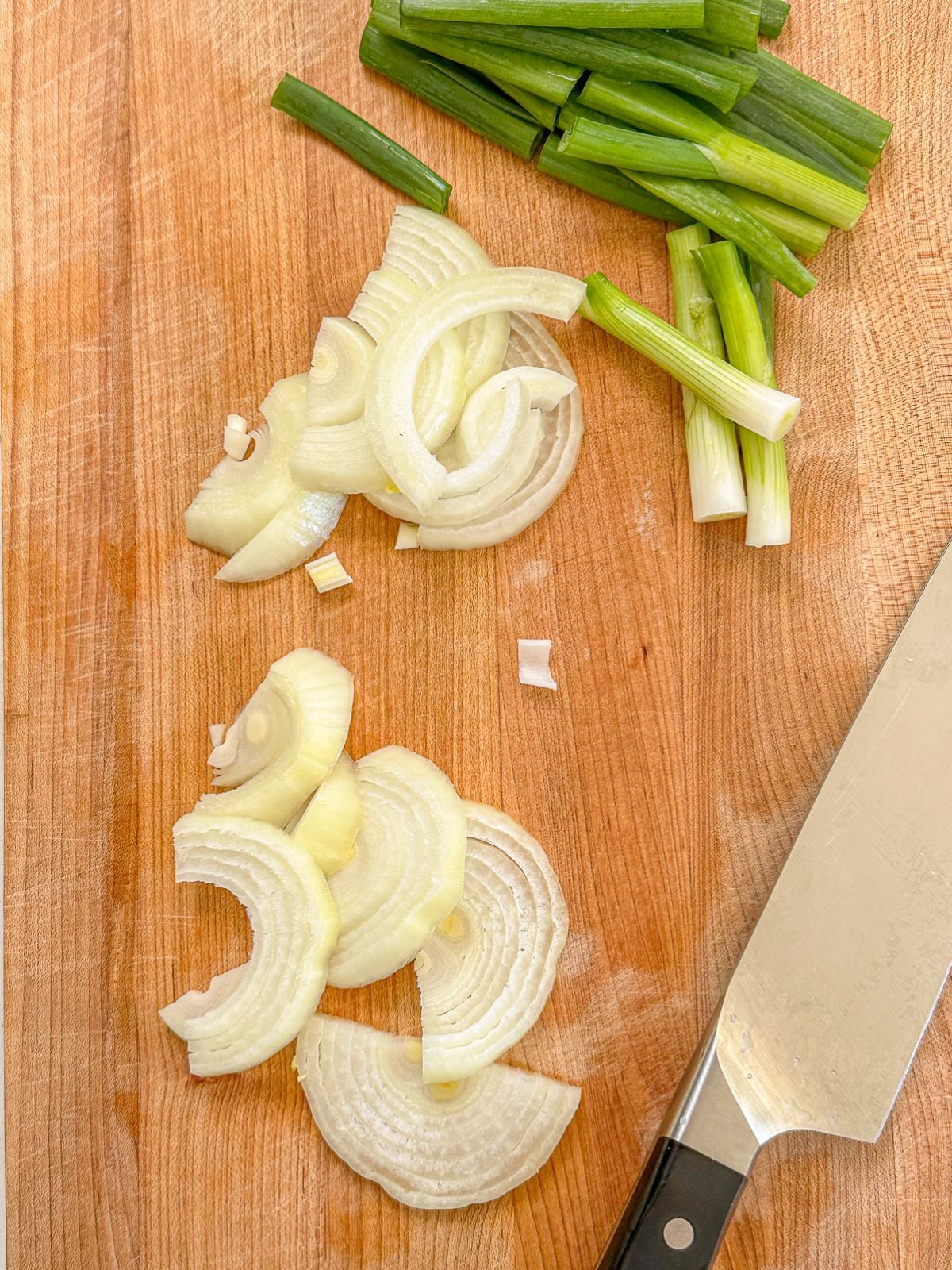 Sliced green onion and white onion on a chopping board.