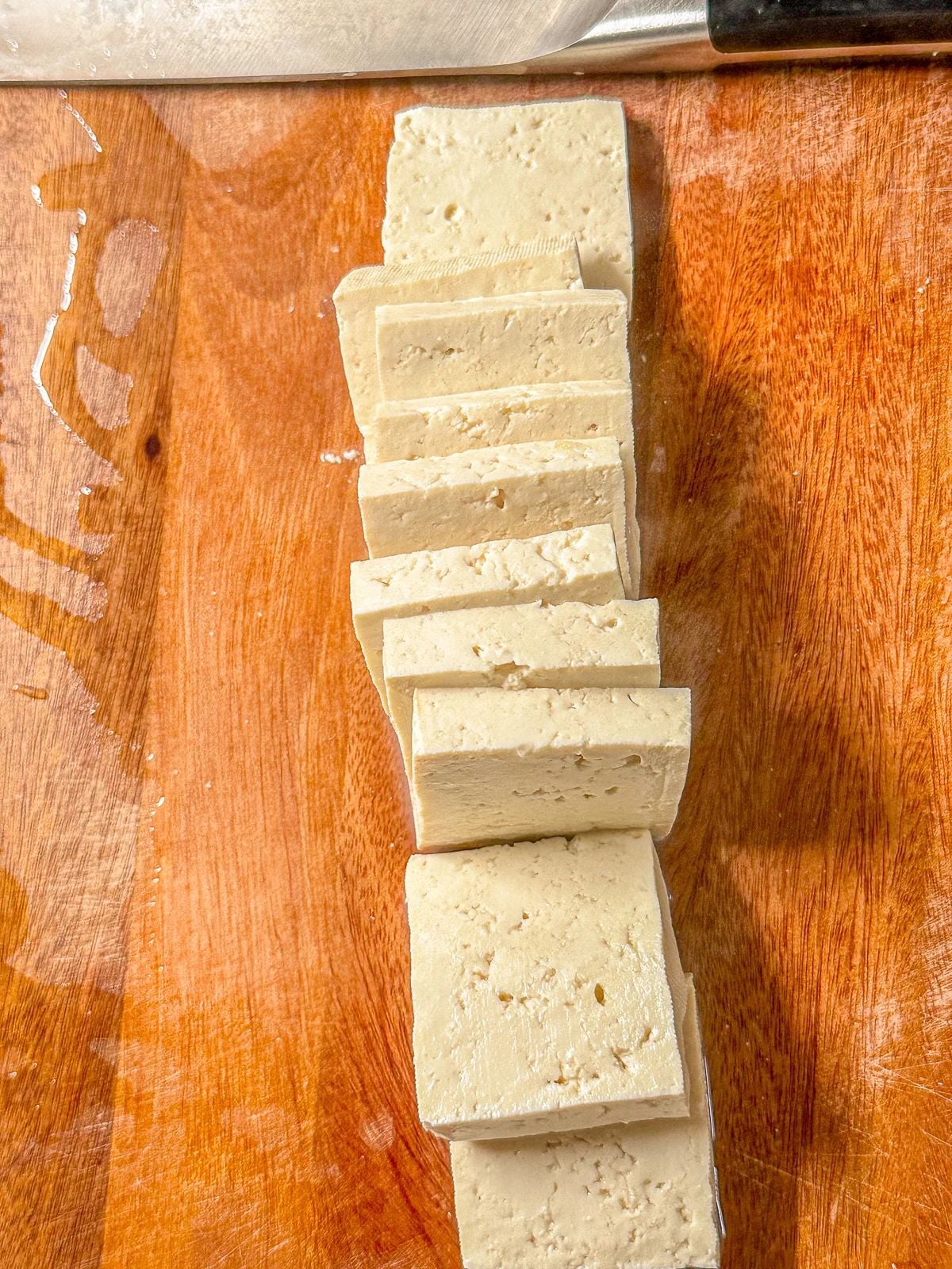 Sliced tofu on cutting board with a knife on the side.