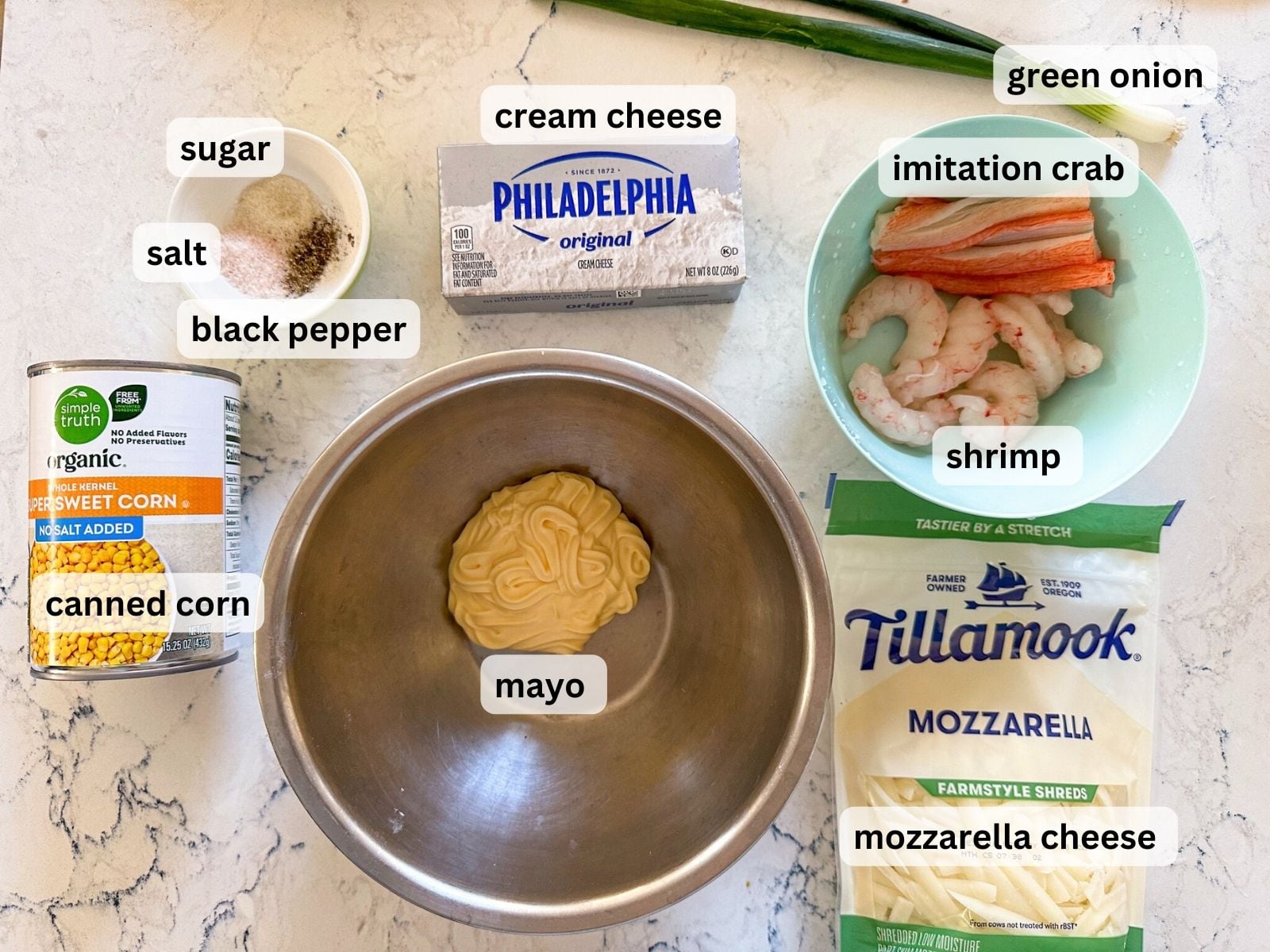 Korean corn cheese dip ingredients laid out on a table countertop including canned corn, mayo, mozzarella, shrimp, imitation crab, cream cheese, green onion and seasonings.