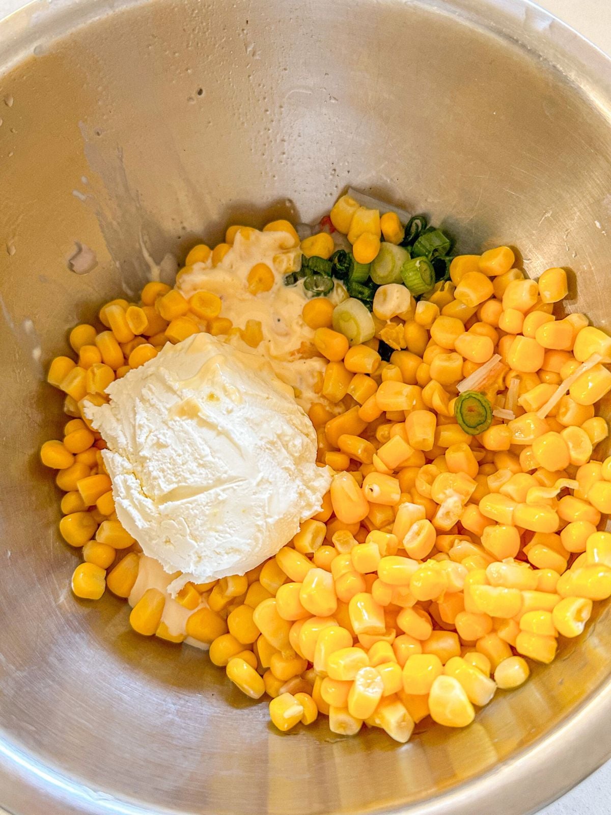 A bowl of corn topped with a dollop of cream cheese and sliced green onions.