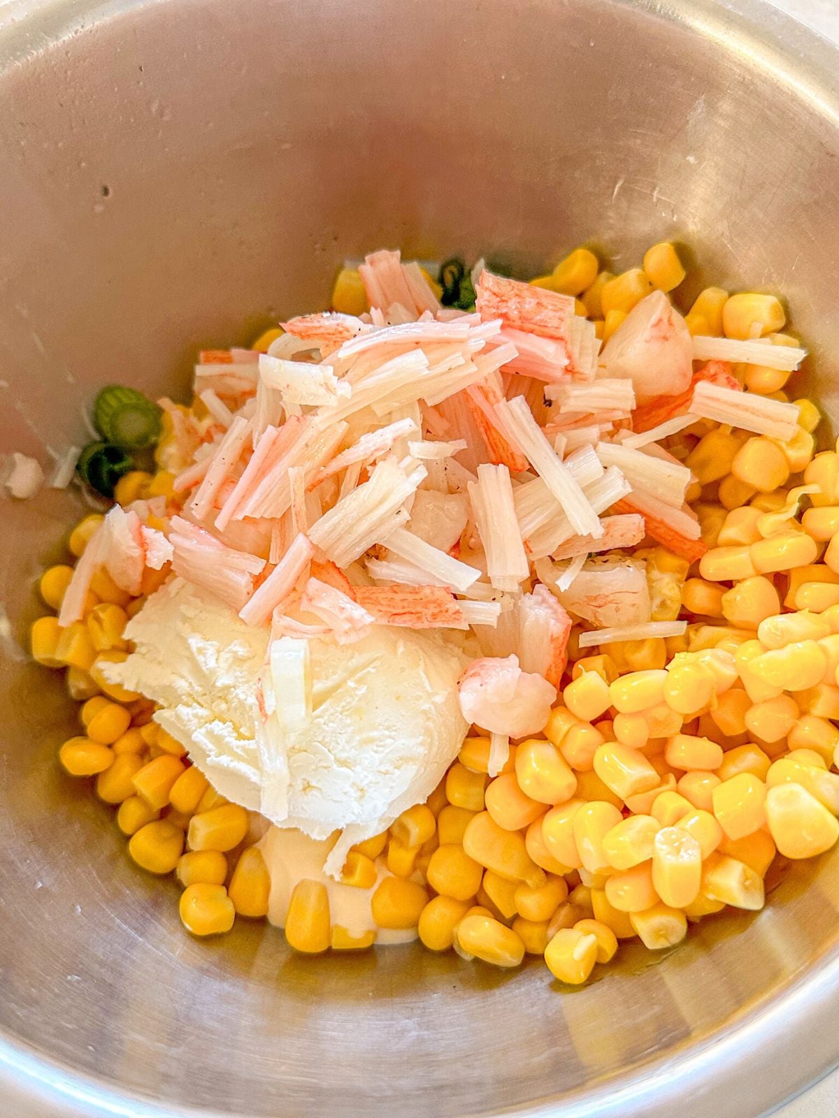 A bowl of corn topped with a dollop of cream cheese and sliced green onions, shrimp and imitation crab.