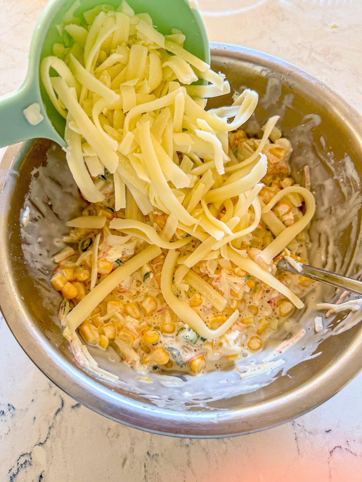 Adding shredded mozzarella on a bowl of corn.