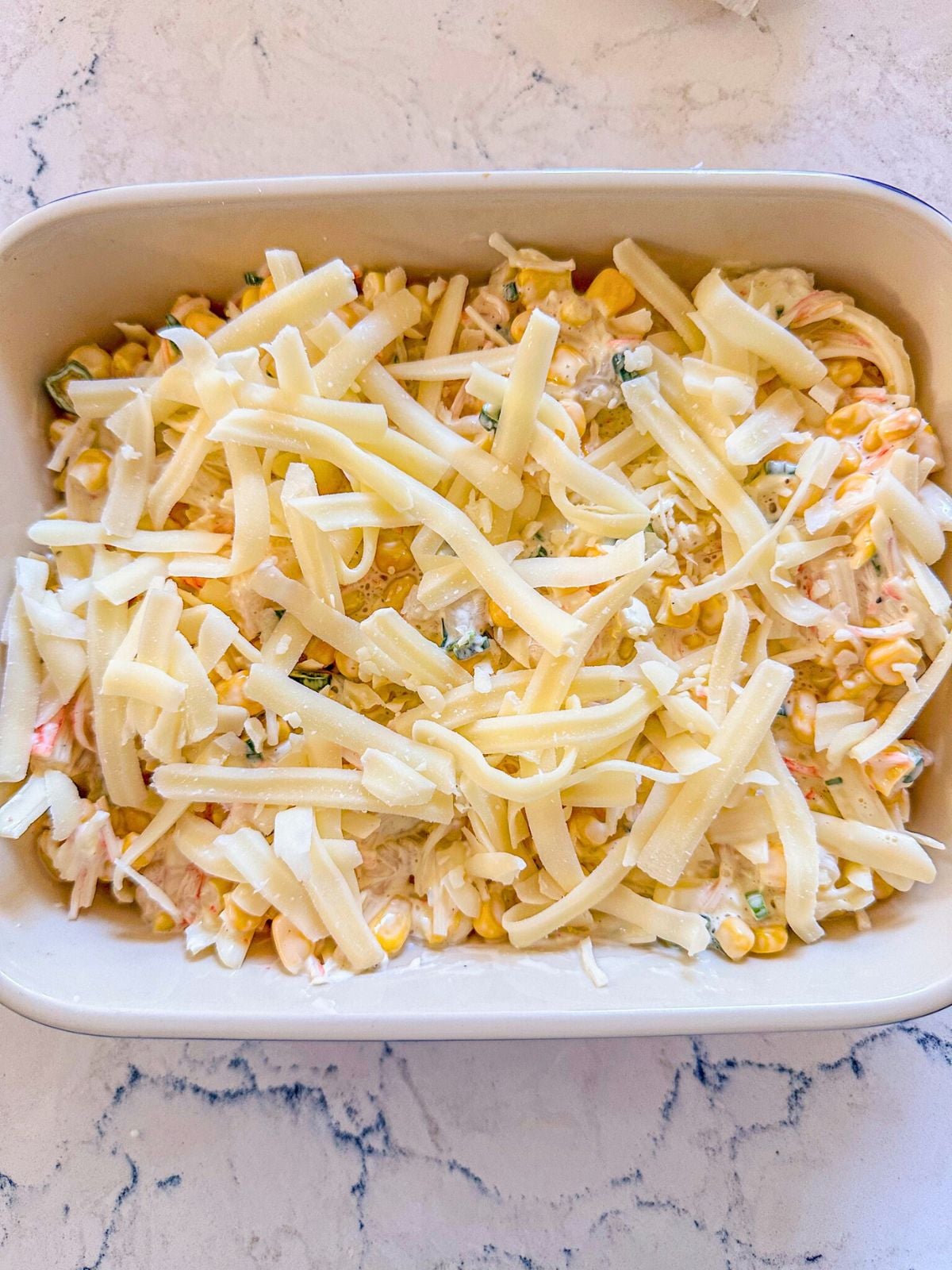 A rectangular baking dish filled with corn mixture and topped with mozzarella cheese.