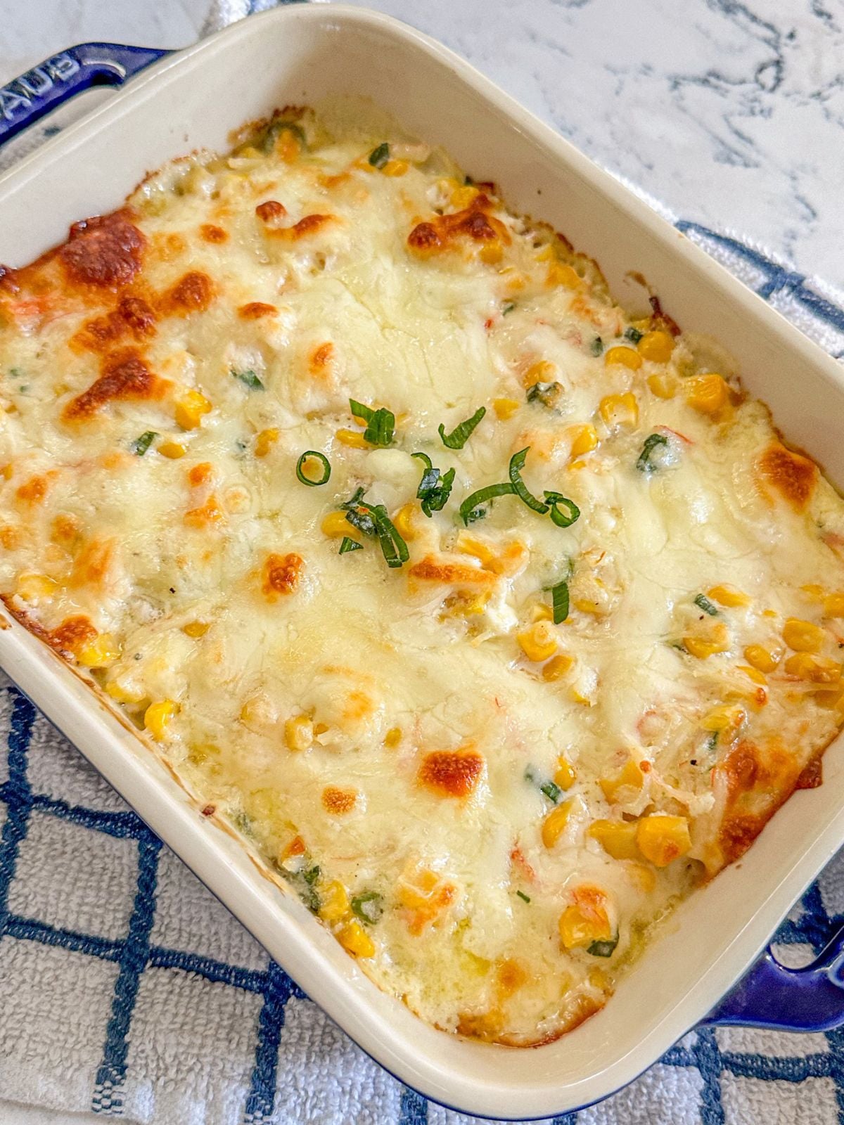 A rectangular baking dish filled with baked corn mixture and finished with melted mozzarella cheese on top.