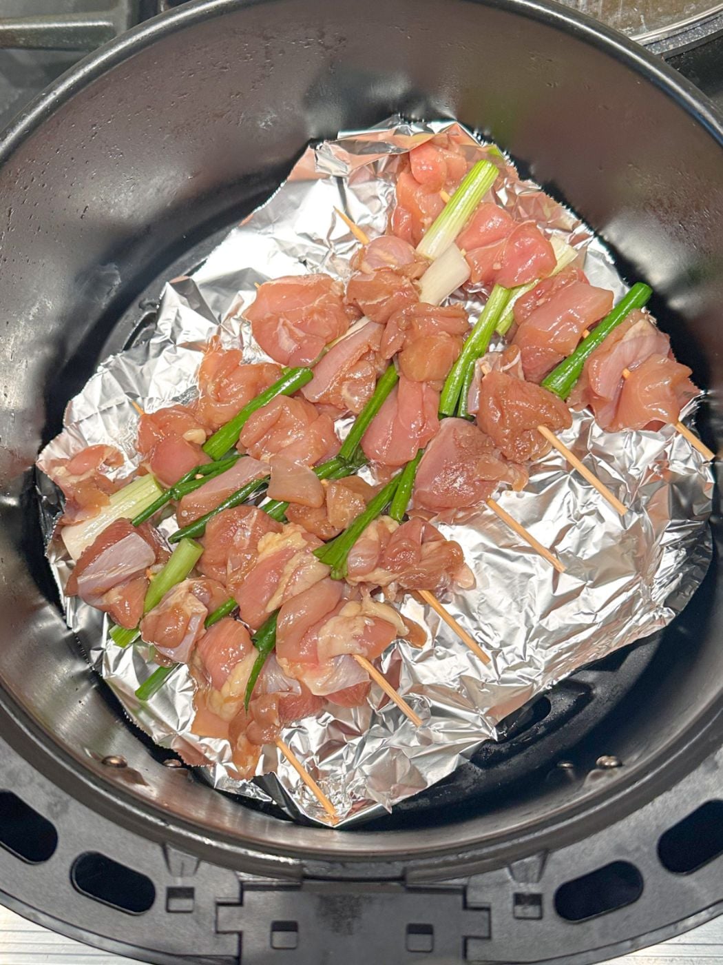 Chicken skewers with green onion in the air fryer basket.