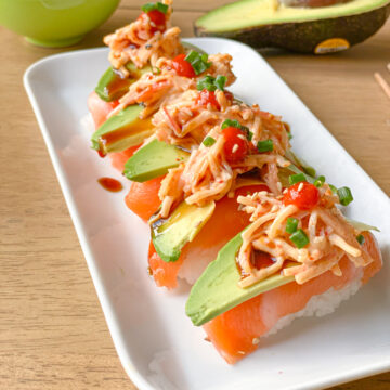 salmon nigiri with spicy crab avocado slices, green onions and spicy red sauce