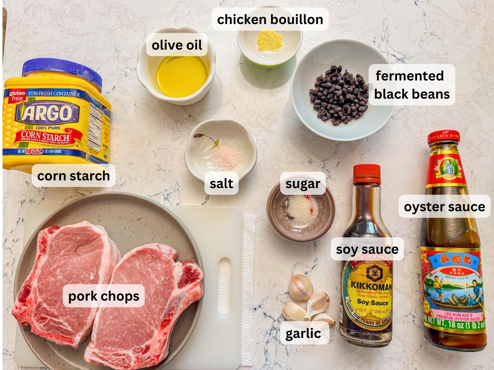 Ingredients for steamed pork with black bean sauce laid out on the table countertop including porkchops, garlic, fermented black beans, corn starch, olive oil and seasonings.