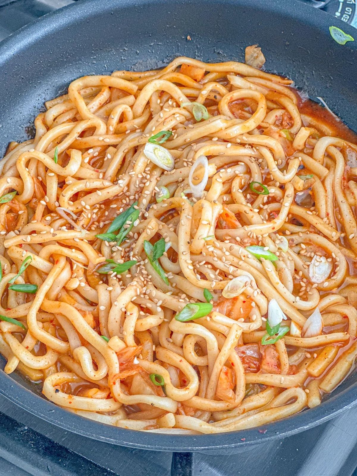 Kimchi red sauce udon with a fried egg and green onions garnished on top.
