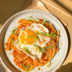 Kimchi udon noodles with spicy sauce, green onions, fried egg on top on a plate.