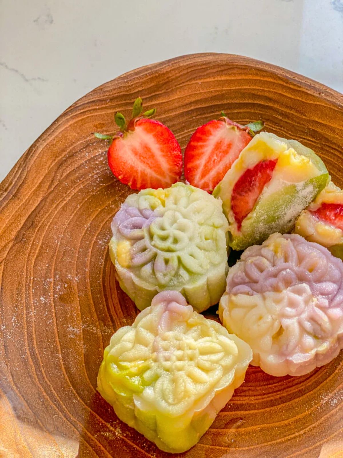 Snow skin mooncakes on a wooden plate, with sliced strawberries on the side.