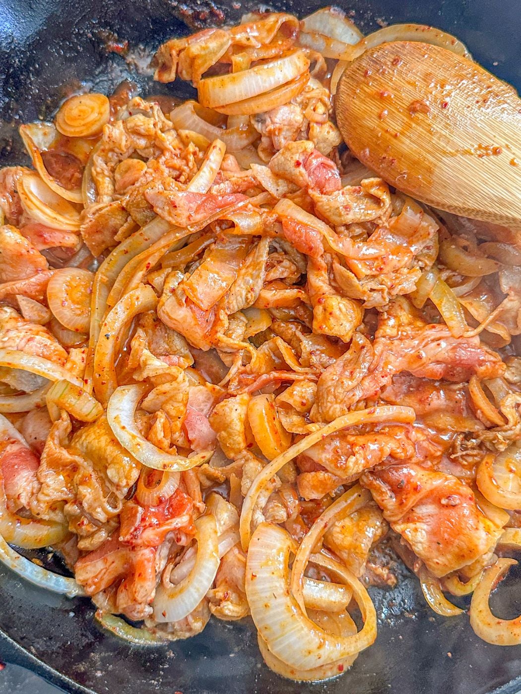 Sliced pork belly sauteed with onions and hot sauce in a pan.