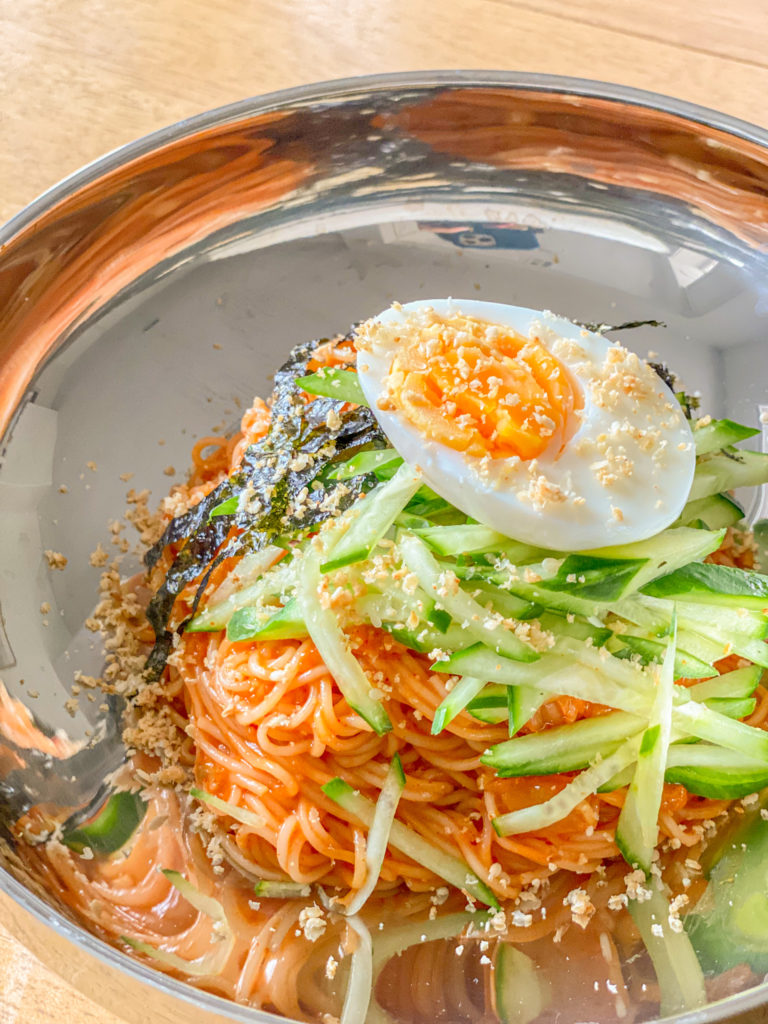 spicy gochujang with kimchi mixed with noodles cucumber and egg on top with sesame seeds