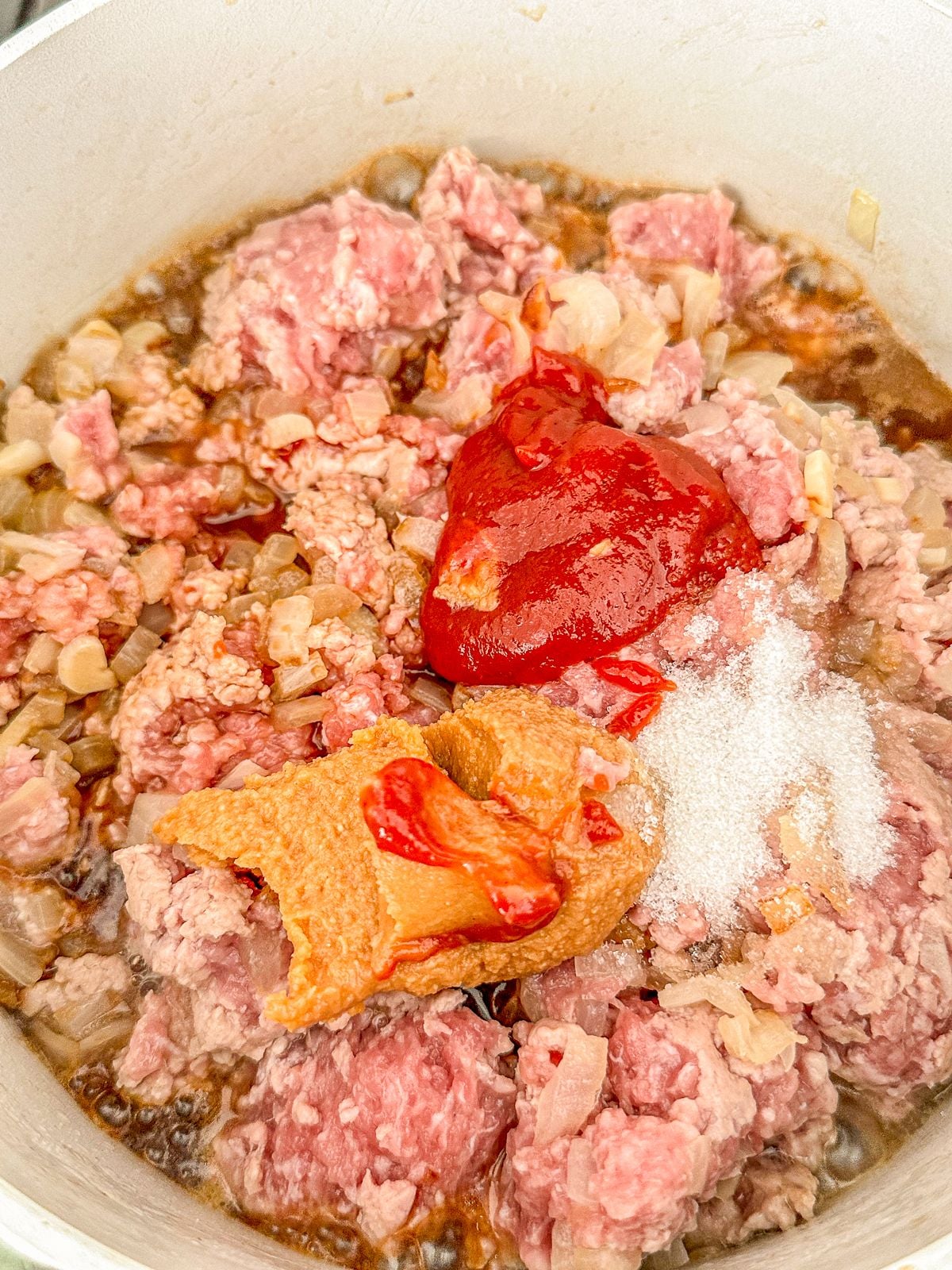 Adding ketchup, miso, sugar to pork and onions in a pot.