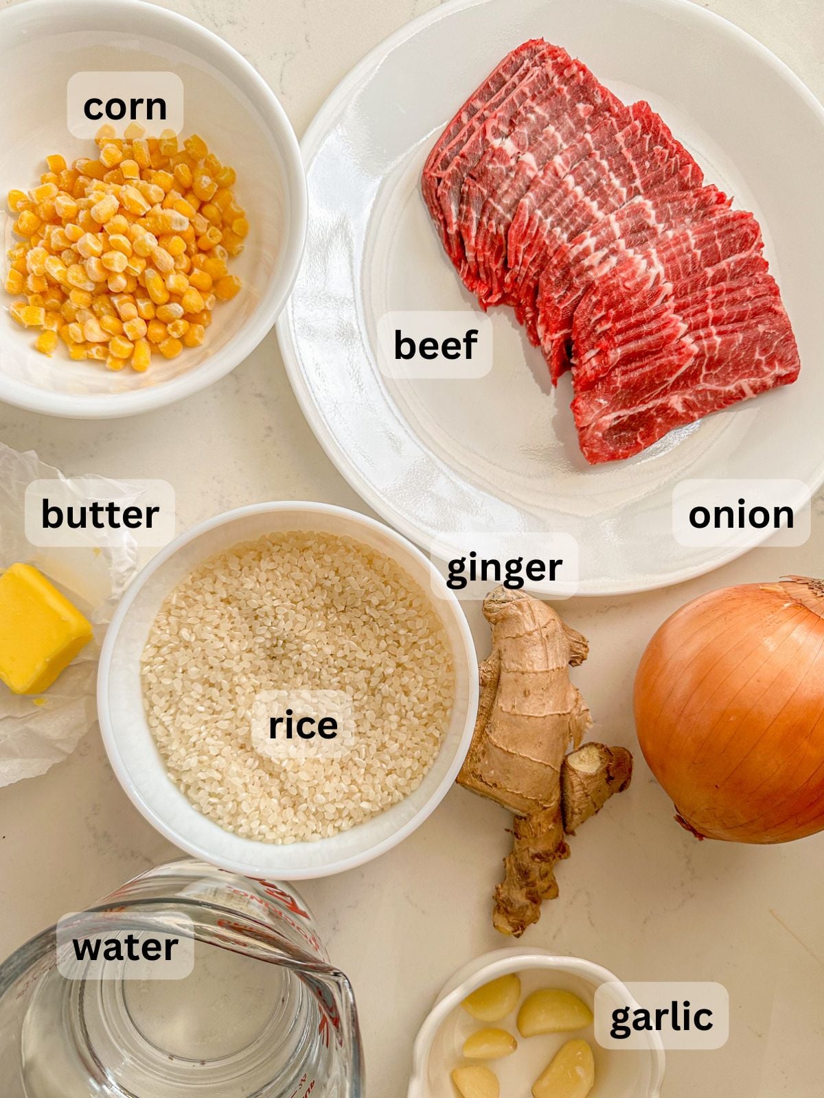 Ingredients with beef, corn, onion, ginger, rice, butter, water and garlic laid out on the countertop.