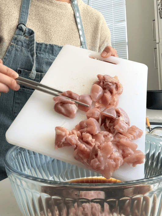 pouring cut chicken in soy marinade bowl