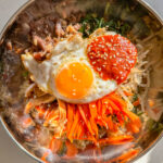 beef, spinach, bean sprouts, carrots, mushrooms and a fried egg in a stainless steel bowl