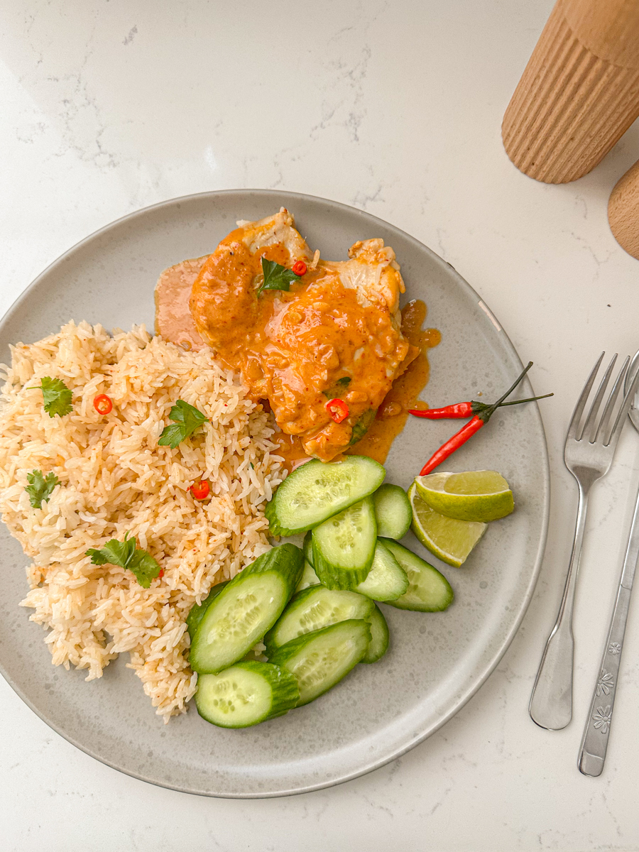 curry chicken on a plate with cucumbers, chili, lime, fork and rice