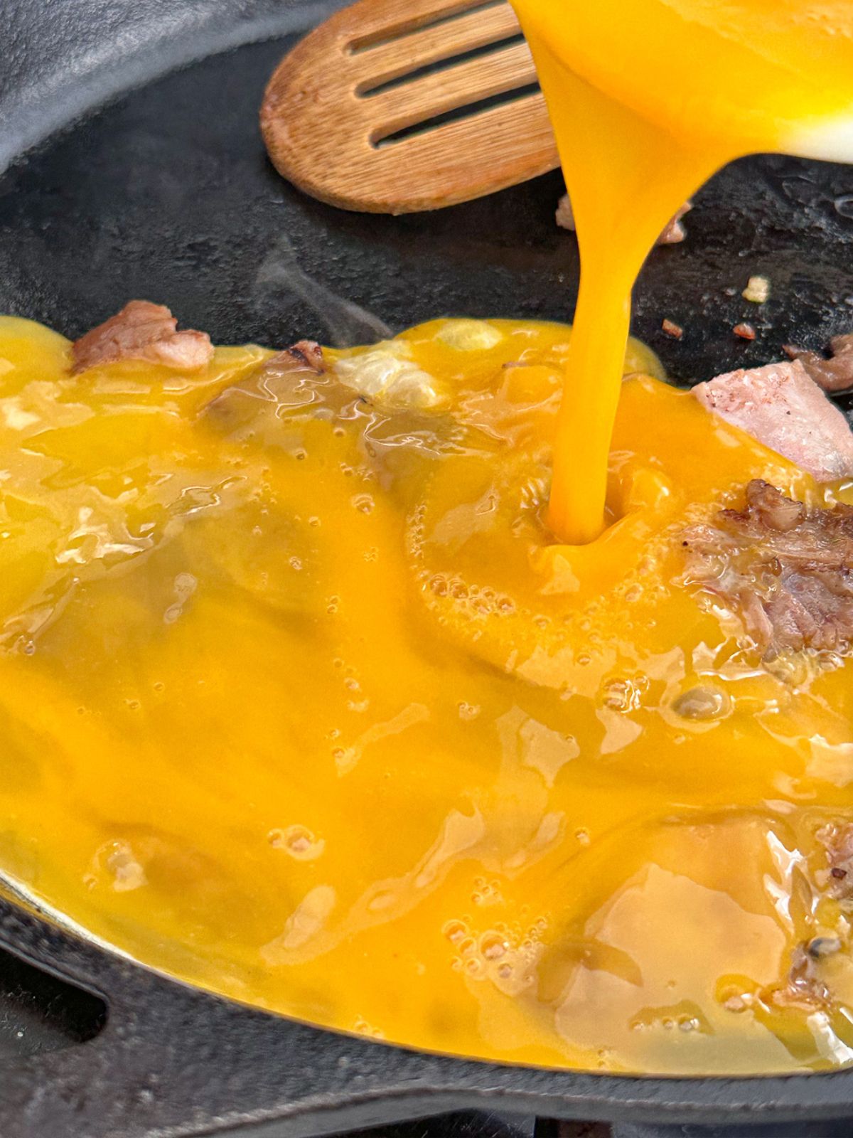 Adding beaten eggs to a pan with pork.
