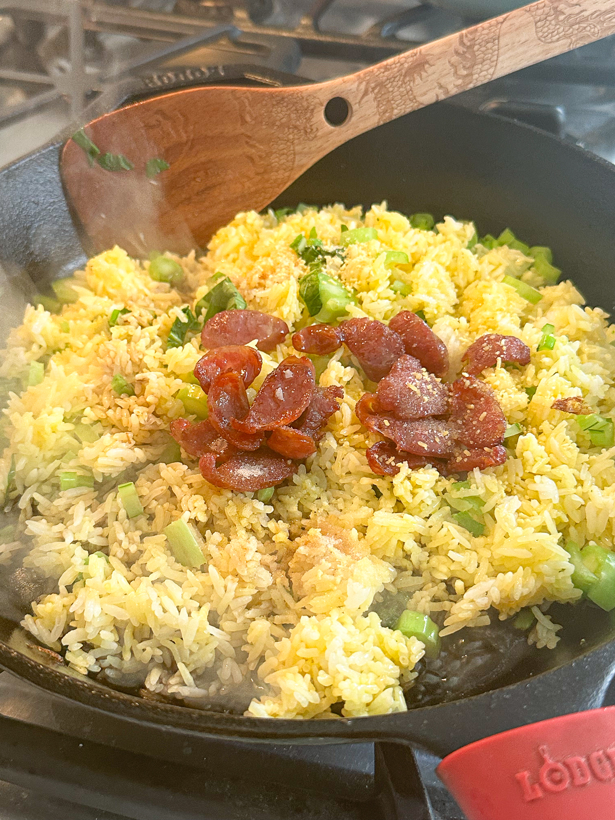 Fried rice with eggs, soy sauce, chicken bouillon, green onions, sausage in a pan with a spatula.