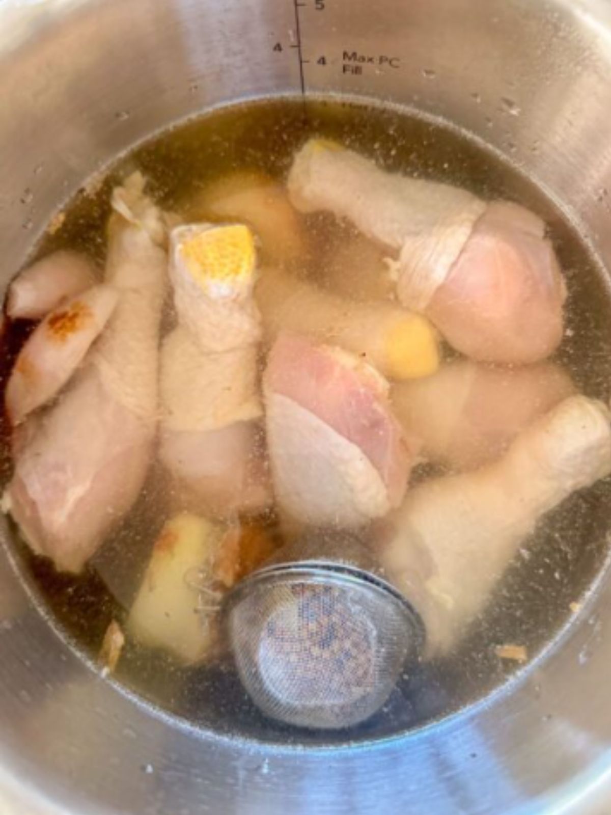 Chicken drumsticks simmering in broth with aromatics and a spice strainer in the Instant Pot.