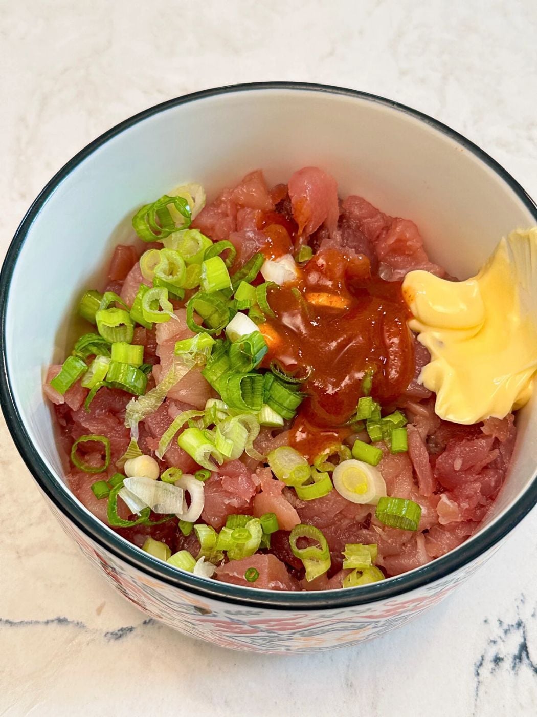 A bowl with minced tuna, sriracha, mayo and sliced green onions.