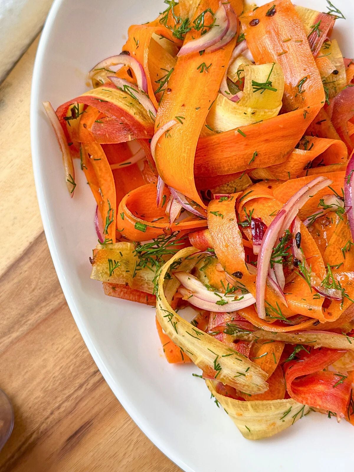 A plate of peeled Carrot salad mixed with red onion, and sprinkled with chopped dill.