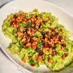 A bowl of guacamole with drizzled chili oil and peanuts on top.