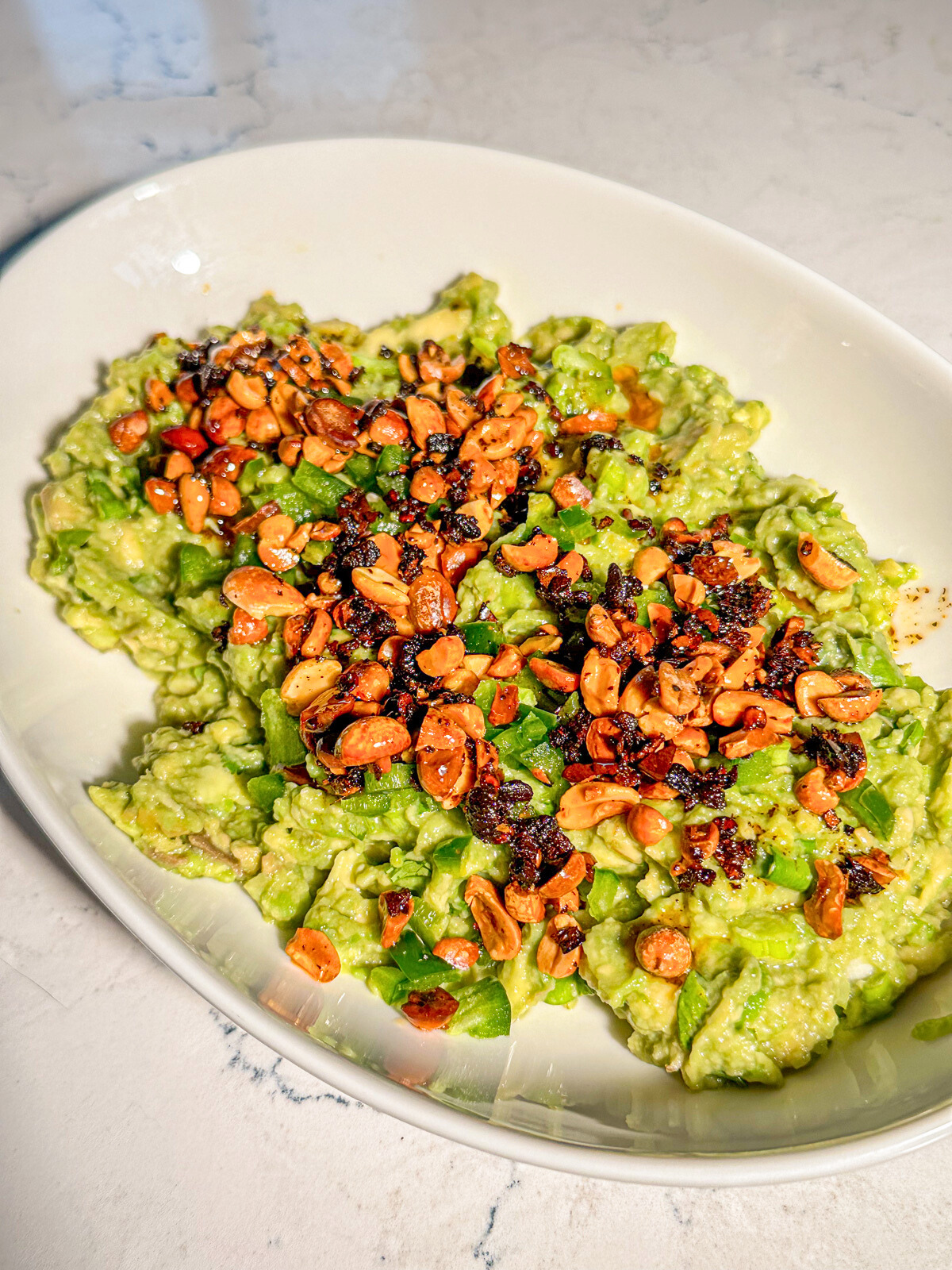 A bowl of guacamole with sprinkled garlic and nuts on top. 