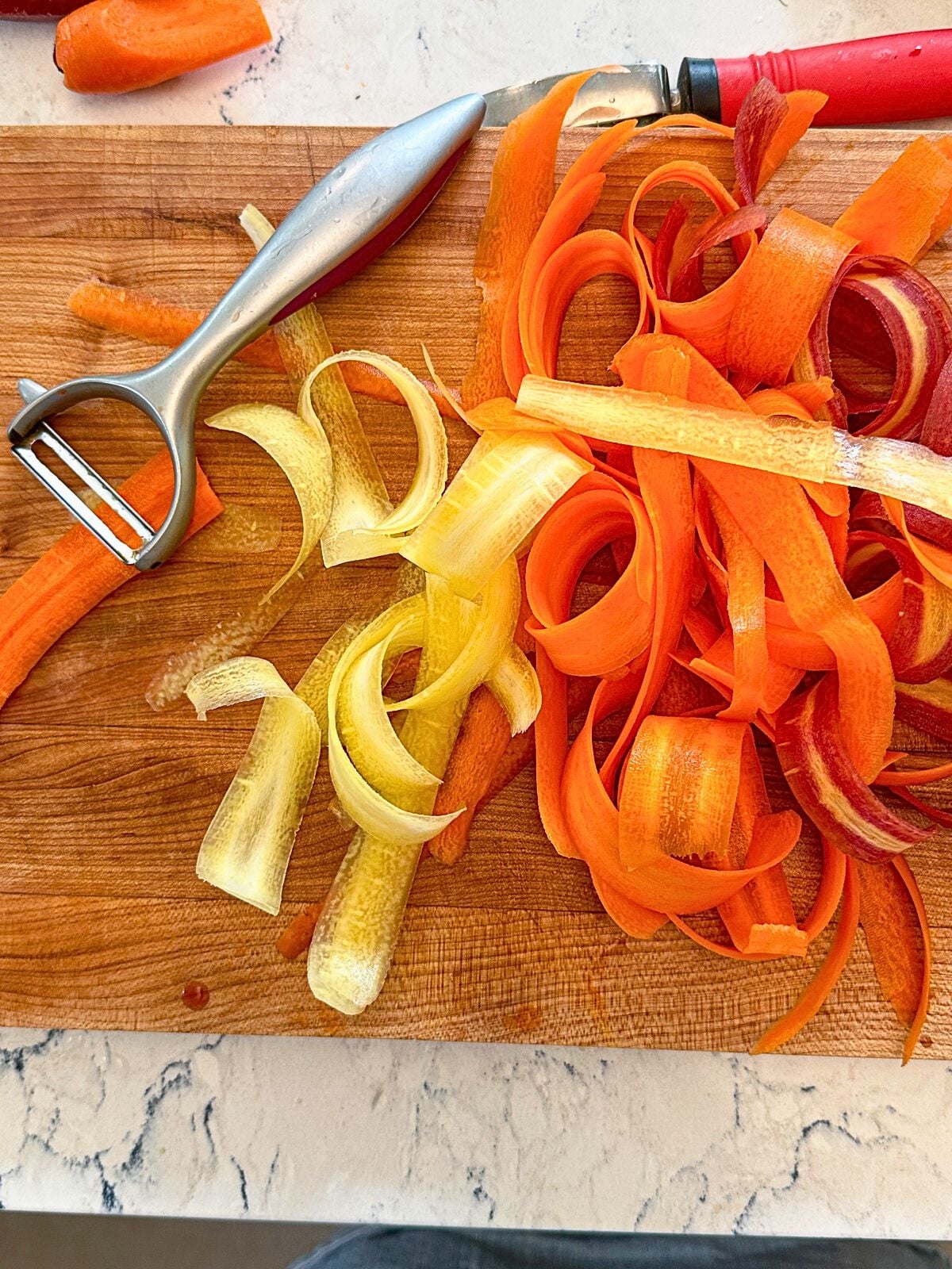 Thin slices of carrots on a chopping board with a grater on the side.