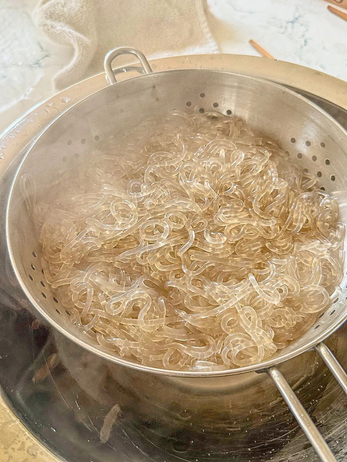 Steamed glass noodles in a metal strainer placed over a pot.