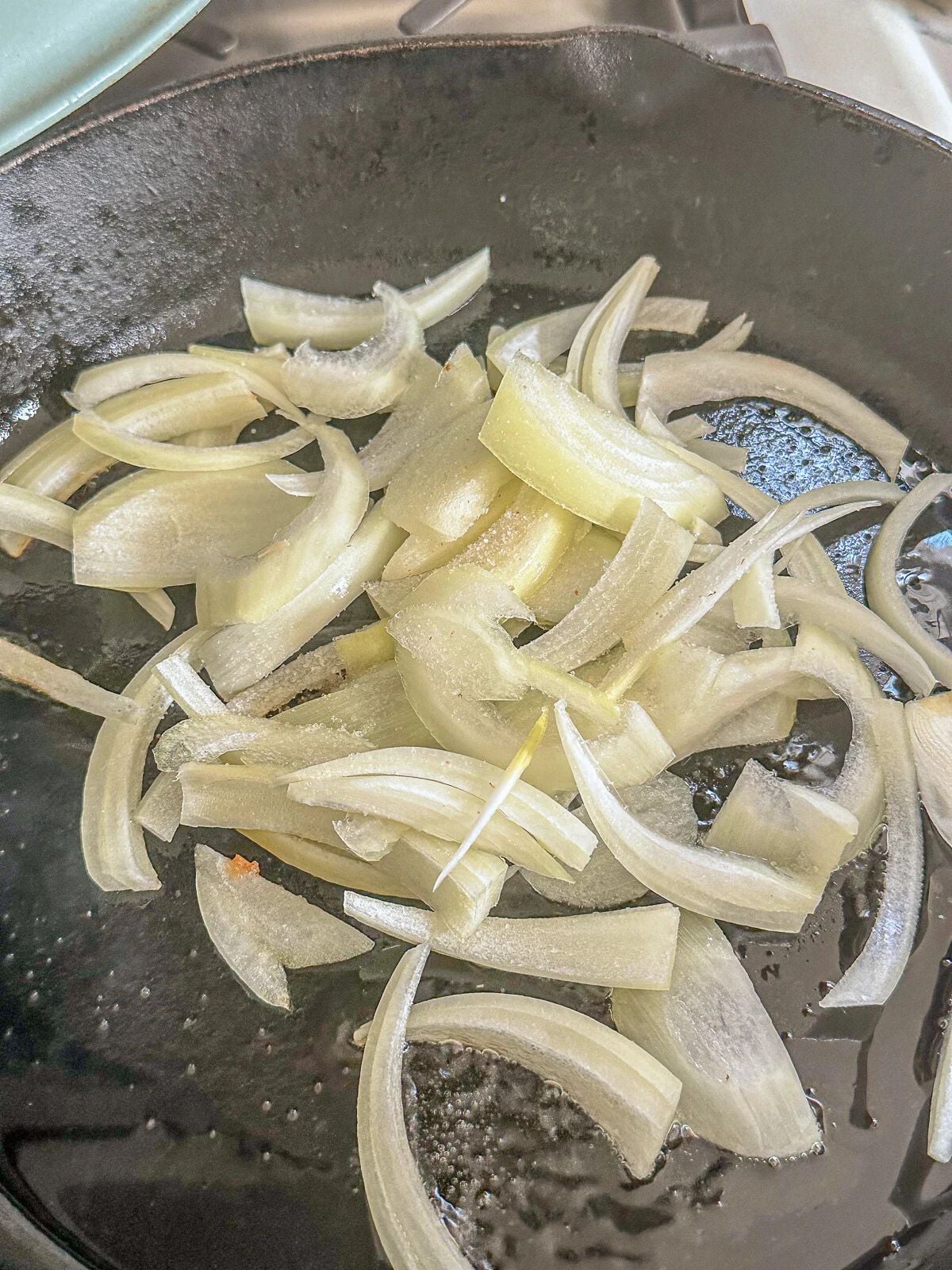 Sliced onions being sautéed in a pan with oil.
