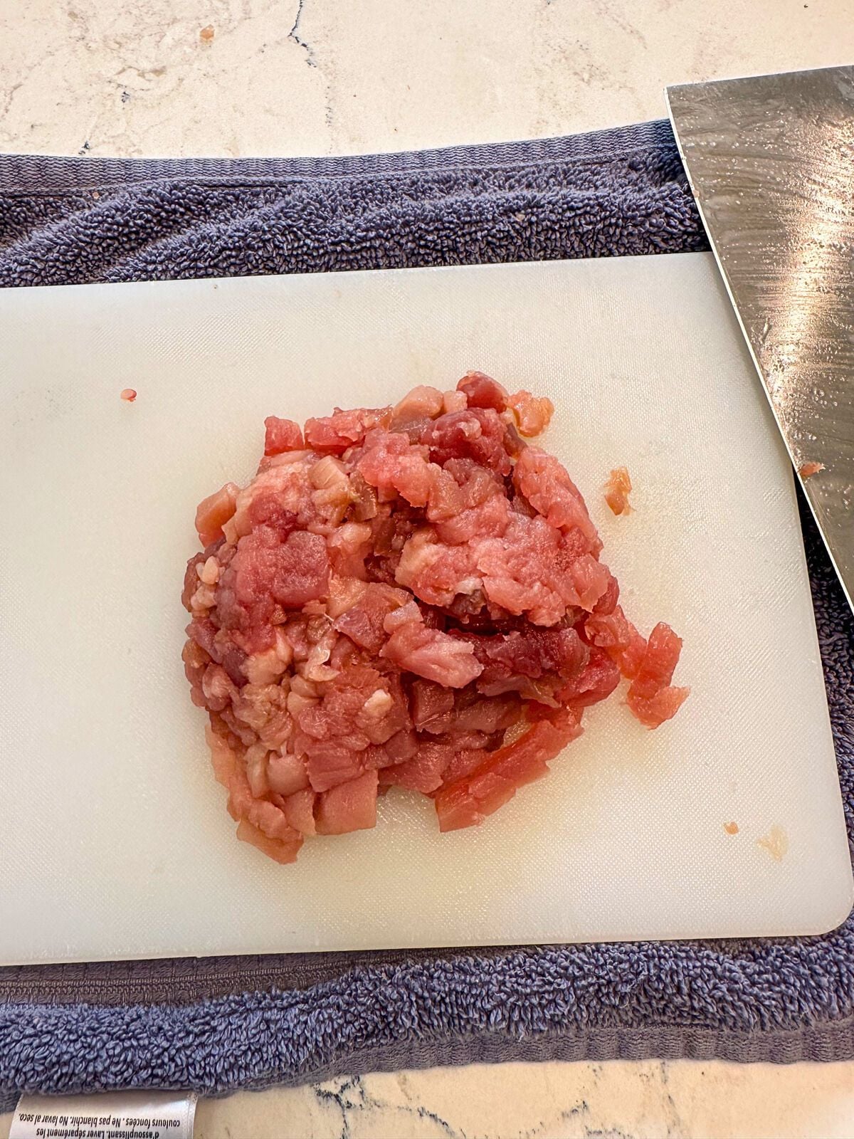 Minced Tuna on a cutting board with a kitchen towel underneath and a kitchen knife on the side.