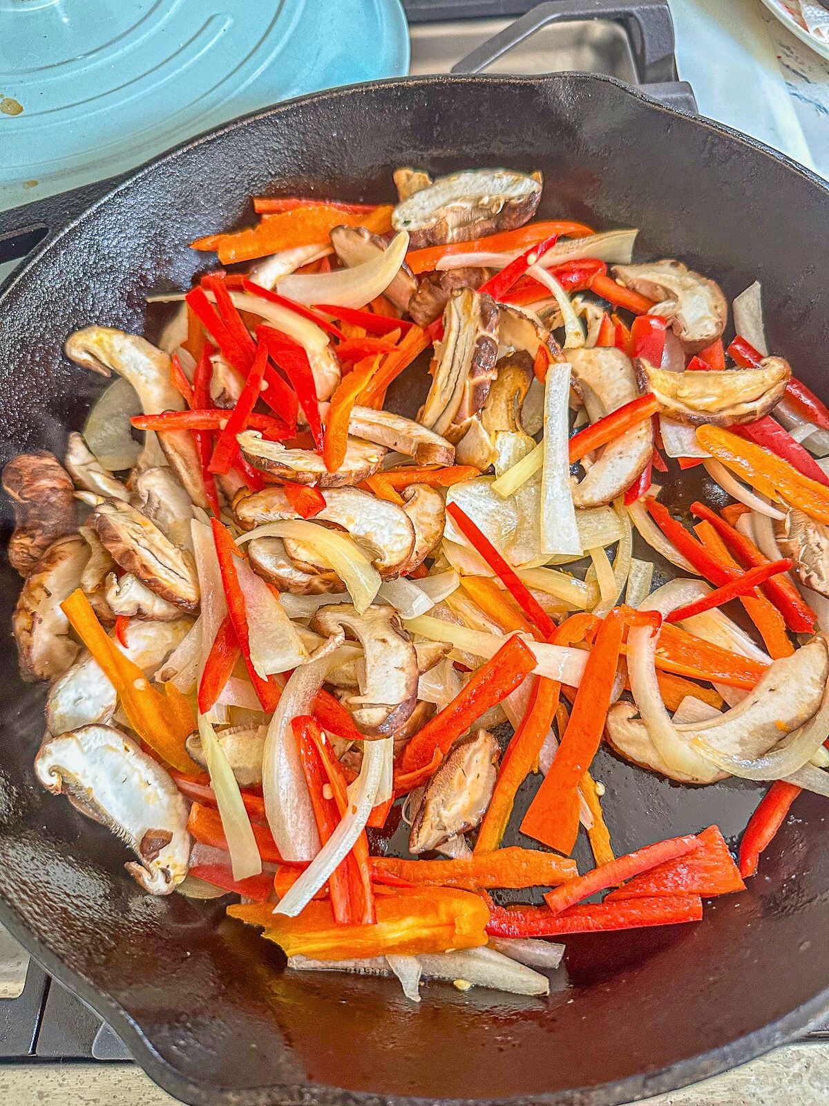 Stir-frying sliced onions, red bell peppers, and shiitake mushrooms in a skillet.