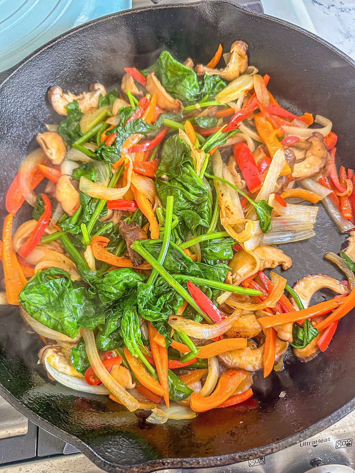 Sautéed vegetables including wilted spinach, bell peppers, onions, and mushrooms in a skillet.