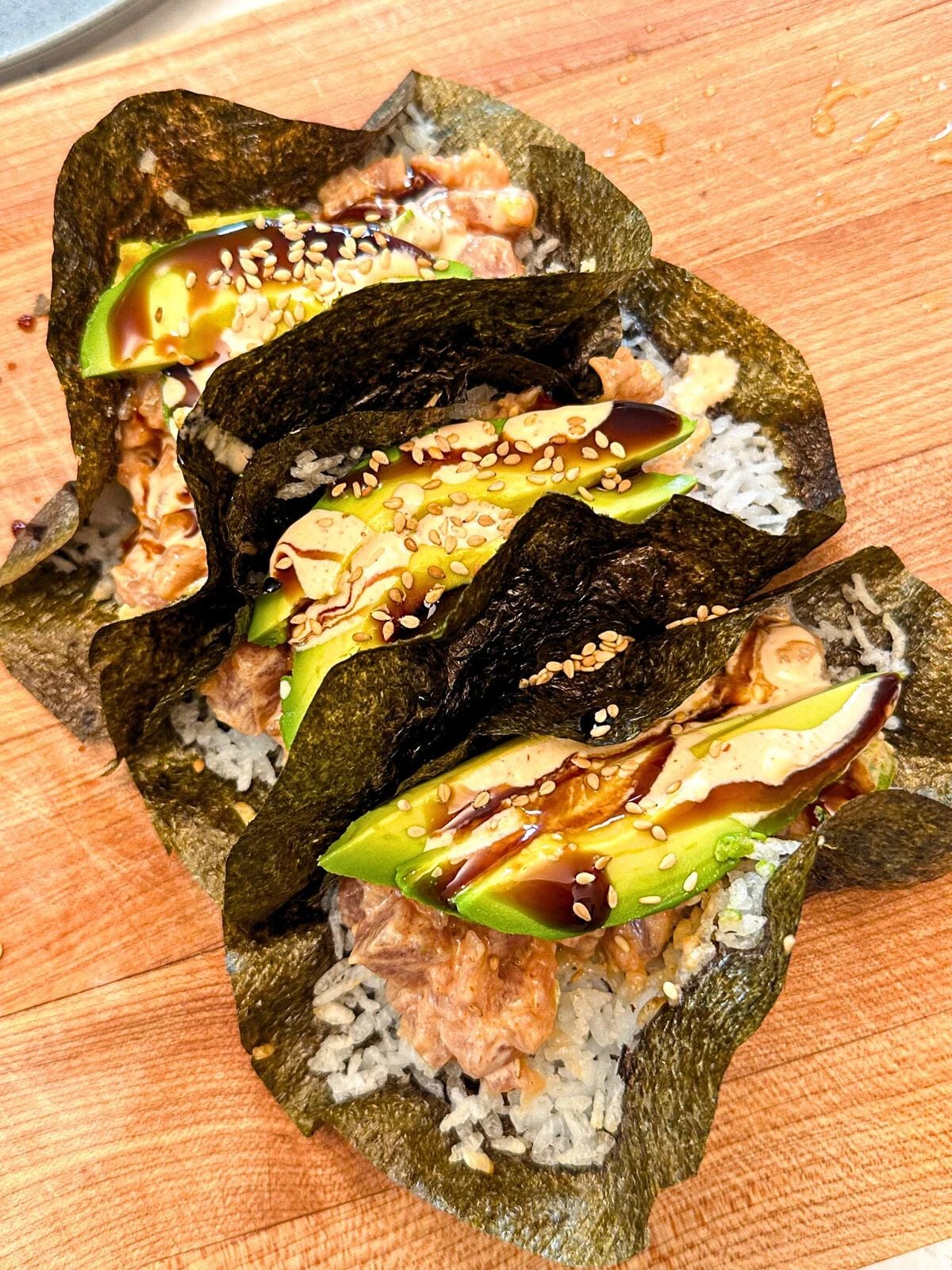 Tuna poke tacos with crispy seaweed shells, rice, tuna, topped with avocado, sesame seeds and teriyaki sauce.