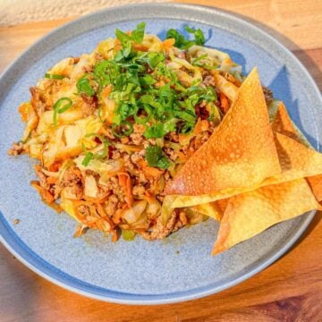 A plate of deconstructed egg roll with garnished cilantro and green onions and wonton chips on the side.