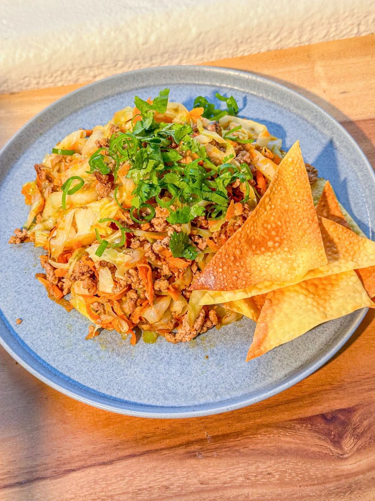 A plate of deconstructed egg roll with garnished cilantro and green onions and wonton chips on the side.