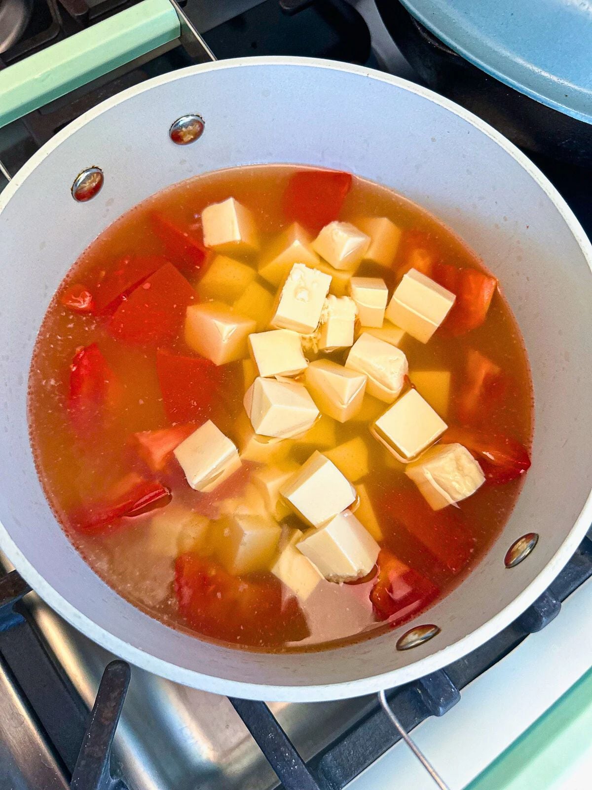 Tomato and tofu chunks in a pot of water.