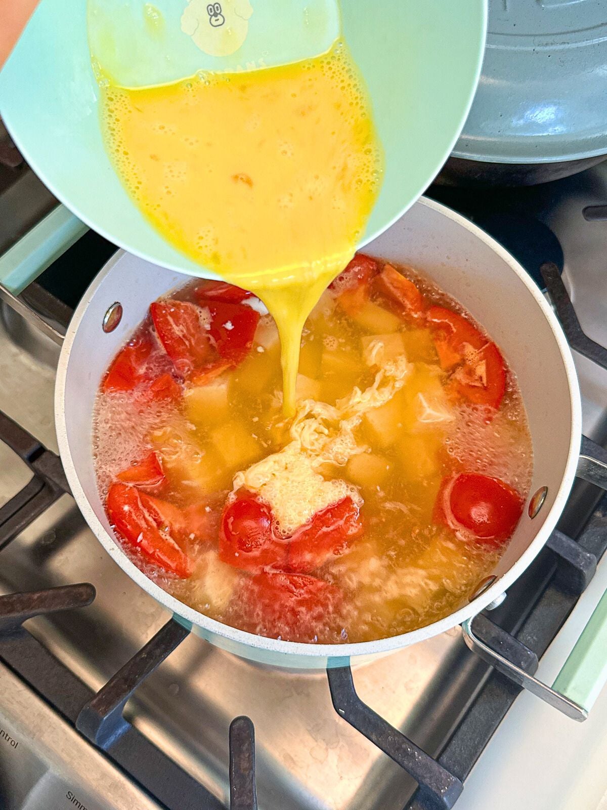 Adding beaten eggs to a pot of tomatoes and tofu simmering in water.