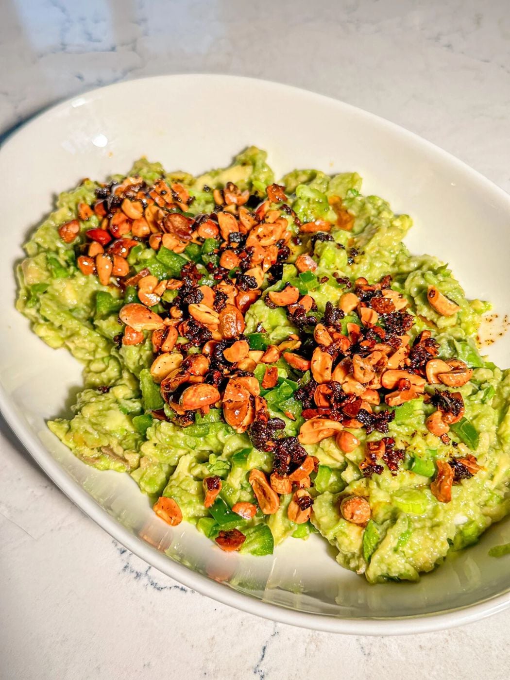 A bowl of guacamole with sprinkled garlic and nuts on top.