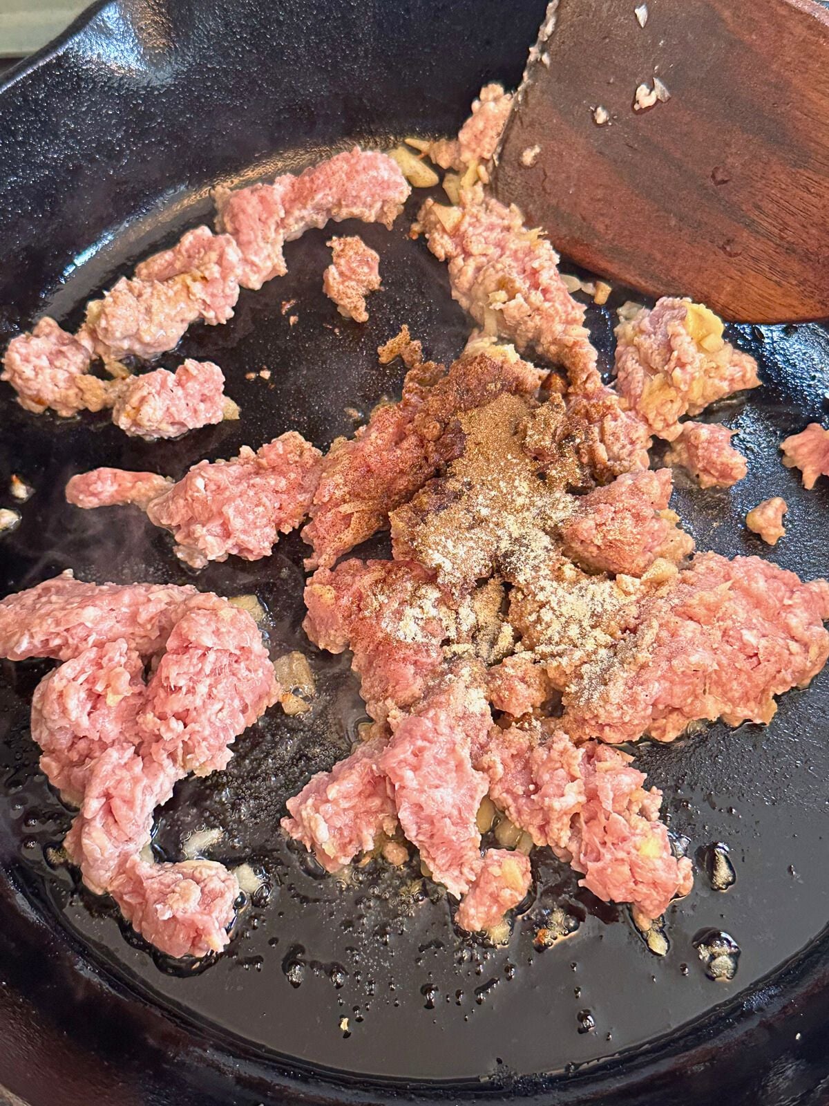 Ground pork in a pan with sprinkled 5 spice and white pepper on top.