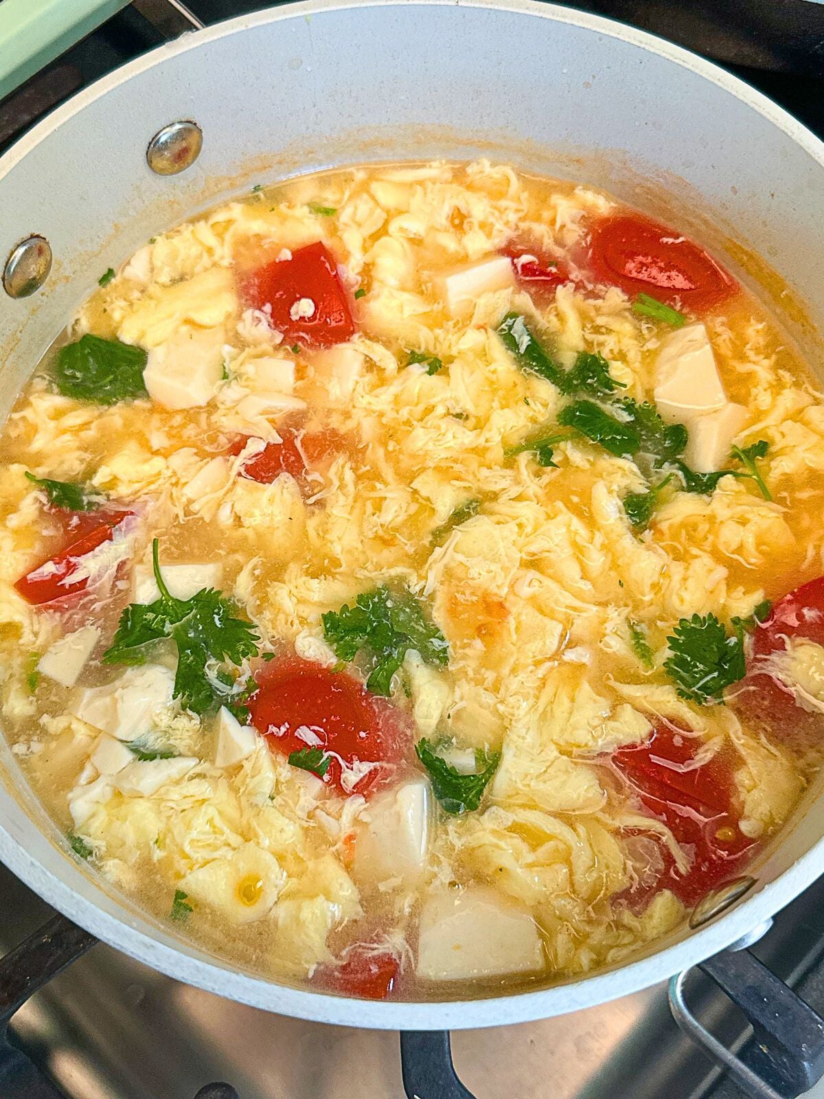 Tomato egg soup with tofu and sprinkled cilantro in a pot.