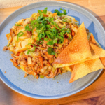 A plate of Egg roll with garnished cilantro and wonton chips on the side.