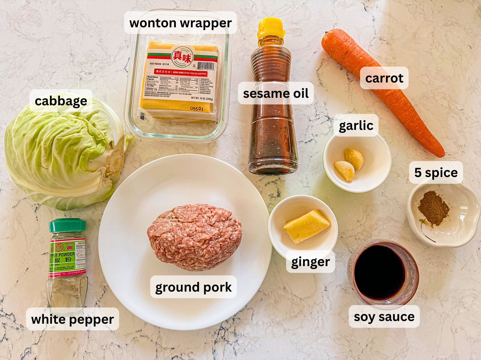 Egg in a bowl labeled ingredients  including wonton wrappers, sesame oil, carrot, cabbage, ground pork, white pepper, ginger, garlic, soy sauce and 5 spice.