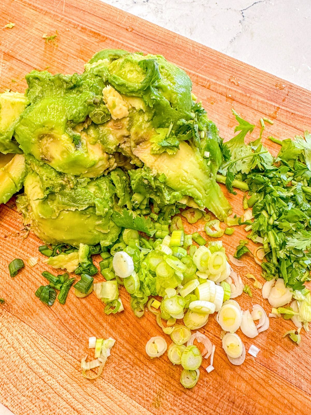 Avocado with chopped green onions and cilantro on the side, placed on a wooden chopping board.